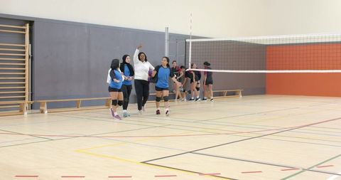 Diverse female volleyball team walking with coach gesturing in school gymnasium