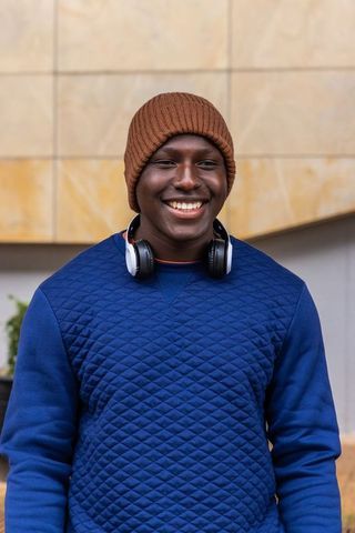 Smiling young man wearing brown beanie and headphones in urban plaza casual portrait style