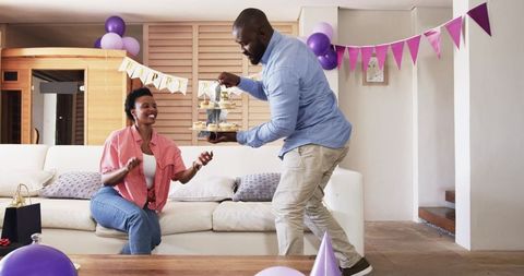 African American couple celebrating birthday at home sharing cupcake tower on sofa