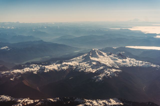 This aerial photo captures a breathtaking view of snow-capped mountain peaks, highlighted by the majesty of nature and the vast expanse of the landscape. Ideal for use in travel blogs, nature magazines, posters, and environmental documentaries. Perfect for conveying the beauty of remote and untouched nature.