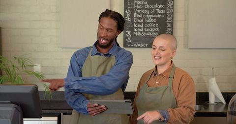 Baristas collaborating at counter pointing to pos while using tablet in modern cafe