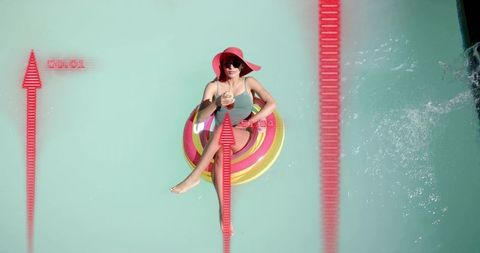 Overhead view woman floating on colorful inflatable donut with sun hat and drink