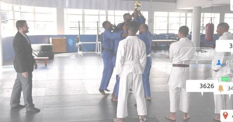 Martial arts team celebrating victory hoisting trophy in dojo with coach watching