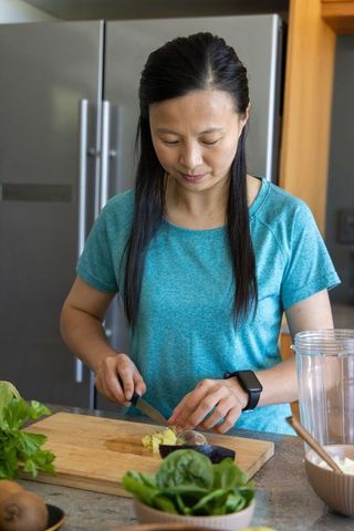 Mature woman chopping produce on kitchen counter preparing healthy green smoothie
