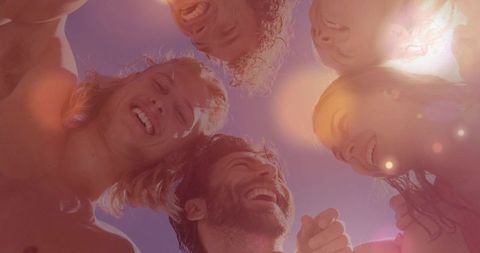 Sunlit friends laughing in overhead circle at poolside beach vacation, candid summer