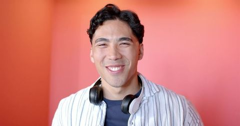 Smiling young man wearing headphones against coral pink backdrop, casual headshot