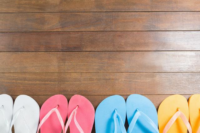 Various pairs of beach flip flops arranged neatly on wooden surface. Perfect for summer vacation themes, travel advertisements, footwear promotions, and casual lifestyle inspirations.