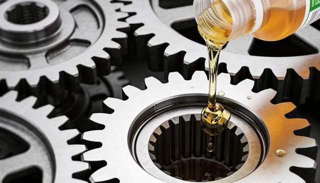 Pouring golden oil into polished spur gear hub for industrial lubrication and maintenance