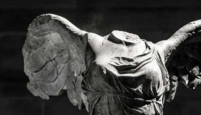 Headless winged marble torso with drapery folds and weathered surface, dramatic black and white