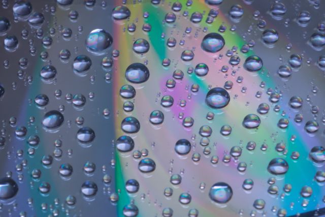 Close-up of water droplets on a vibrant and colorful surface, capturing reflections and soft hues. Useful for design concepts, background textures, or artistic projects where color and detail are important.