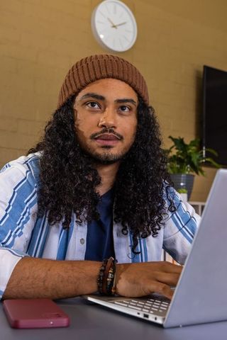 Young man working on laptop in cozy home office wearing beanie and bracelets