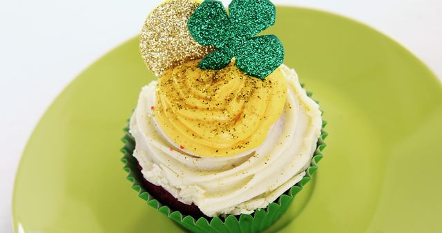 Single cupcake decorated for St. Patrick's Day on green plate. Green wrapper, yellow and white frosting, glittery shamrock and gold coin decorations. Appropriate for St. Patrick's Day marketing, bakery promotions, holiday recipe blogs, festive decor ideas.