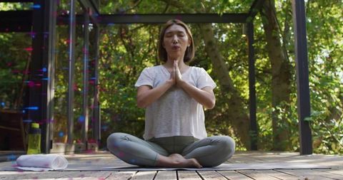 Chinese woman meditating on sunlit wooden deck under pergola practicing mindfulness