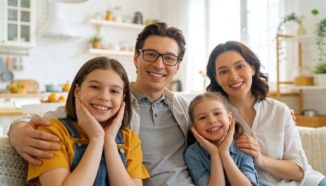 Smiling family sitting together on sofa in sunlit modern open-plan living room with parents smiling
