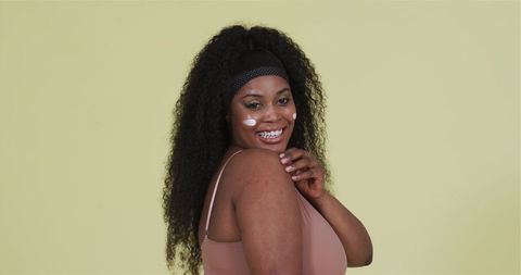 Happy woman applying facial cream stickers yellow background