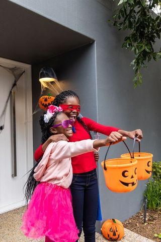 African american preteen girls celebrating halloween on porch holding pumpkin buckets