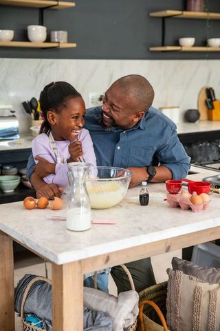 African american father and daughter laughing while whisking batter at marble kitchen island