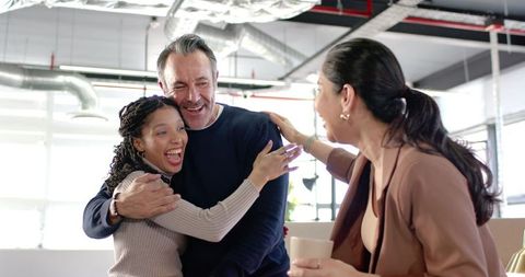 Diverse team laughing and embracing in modern open-plan office during team celebration