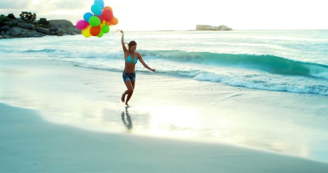 Image captures a young woman holding colorful balloons while running along a sunlit beach. The ocean waves and the sandy shore create a lively and carefree atmosphere. This image can be used for themes of joy, freedom, summer vacations, and outdoor fun. Perfect for travel advertisements, holiday promotions, and summer lifestyle blogs.