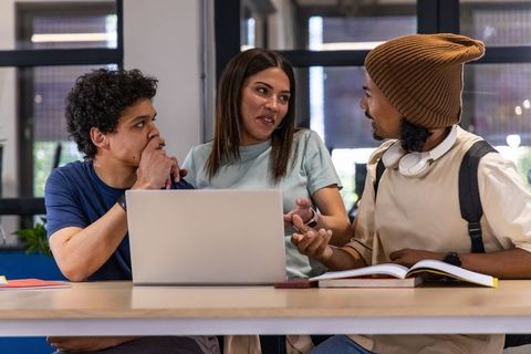 Diverse students collaborating around laptop and open textbook in modern study space