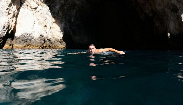 Swimming solo in sunlit sea cave with dramatic limestone cliffs and deep blue water