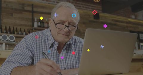 Senior man working on laptop taking notes in cozy coffeehouse casual business scene