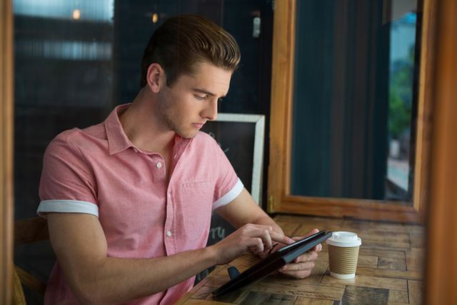 Young man using digital tablet at table in coffee shop