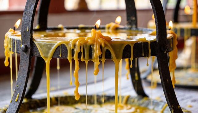 Melting golden wax dripping from round iron candle stand with glowing votive flames