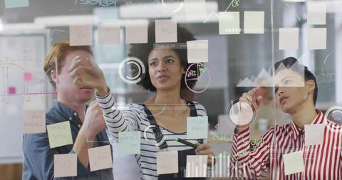 Diverse office team collaborating at glass wall with colorful sticky notes and analytics