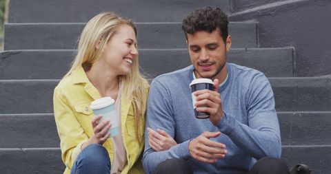 Happy couple enjoying coffee on city stairs