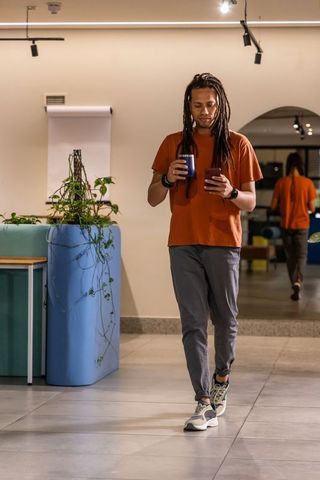 African american man walking through modern coworking lounge holding phone and mug