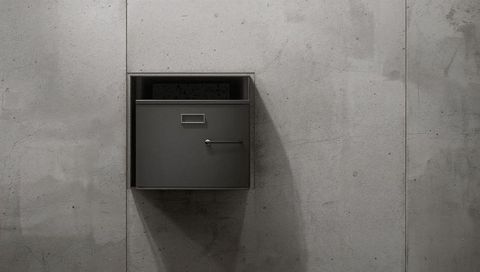 Minimalist industrial wall-mounted drop box recessed in concrete with shadow and texture