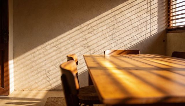 Sunlight Casting Diagonal Blind Shadows Across Wooden Dining Table With Woven Chairs