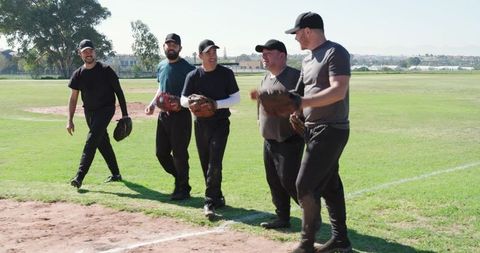 Men Walking Across Baseball Field Smiling and Chatting While Carrying Gloves and Caps