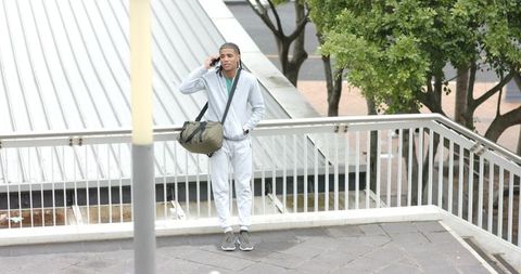 African american man talking on phone at urban overpass wearing tracksuit with duffel bag