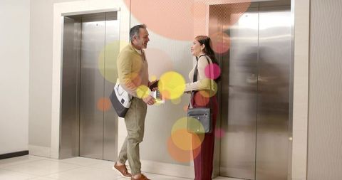 Friendly colleagues chatting in modern office lobby beside stainless steel elevators