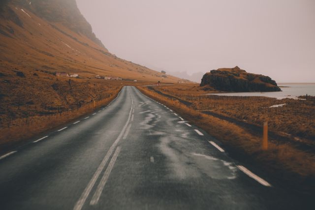 Misty road stretches towards the horizon alongside a rugged coastline in Iceland. The scene evokes a sense of solitude and tranquility, perfect for travel blogs, nature-related projects, adventure themes, or use in articles focusing on remote landscapes and peaceful journeys.
