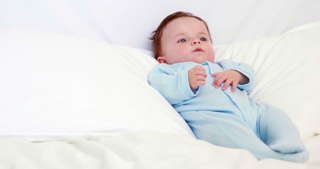 Baby boy in blue babygro lying on pillows at home in bedroom