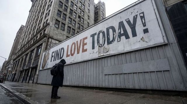 Solitary figure facing weathered find love today billboard on rainy deserted urban sidewalk