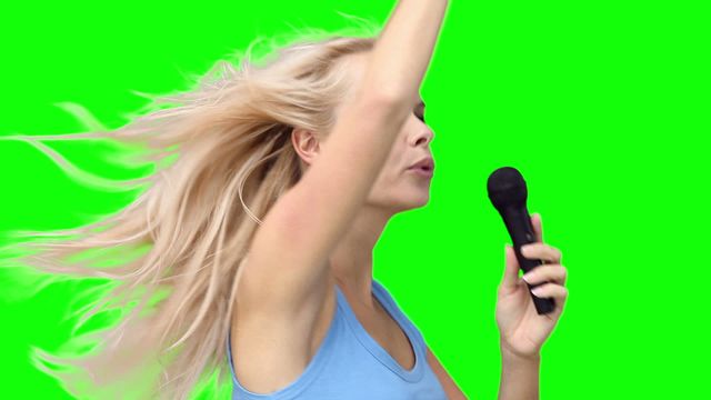 Blonde woman dancing energetically while singing into a microphone, with green background that can be easily replaced in post-production. Ideal for music promotions, concert advertisements, entertainment content, and creative projects requiring vibrant, dynamic images of performers.