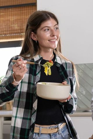 Young woman eating fresh salad with chopsticks in cozy kitchen light