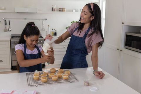 African american mom guiding daughter frosting cupcakes and decorating with sprinkles