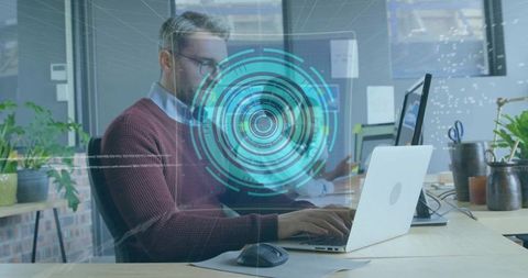 Typing mature man using laptop with holographic cyber interface in modern open-plan office