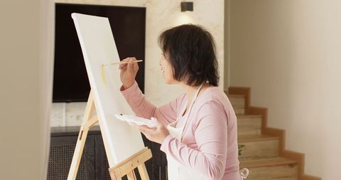 Senior Asian Woman Painting on Canvas in Cozy Living Room
