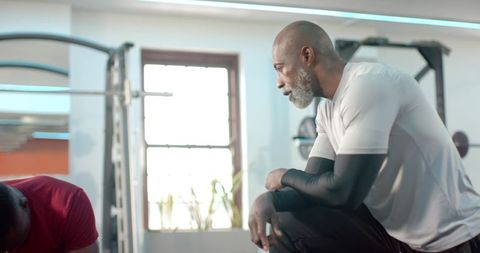 Senior african american trainer coaching client near squat rack in bright gym