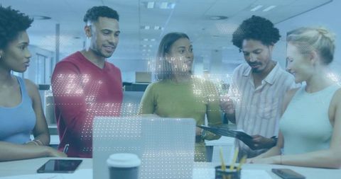 Diverse team collaborating over laptop and tablet in modern open-plan office