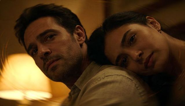 Moody intimate couple leaning together in warm lamp glow, close cinematic portrait of affection