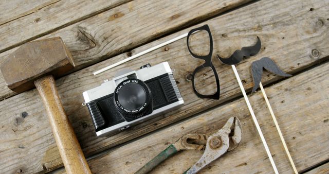 A vintage camera, a pair of glasses, a hammer, and other tools are laid out on a wooden surface, with copy space. These items evoke a sense of nostalgia and creativity, suggesting a blend of photography and craftsmanship.