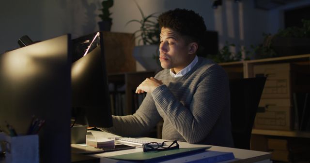 Image of tired biracial man with coffee using computer, working late in office. Business and working in office at night with technology concept.