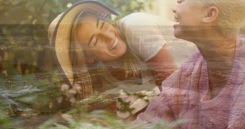 Smiling friends relaxing in sunlit garden with straw hat and ocean double exposure overlay